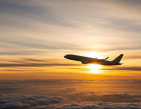 An airplane ascends into the sky as the sun sets during golden hour casting a warm glow.